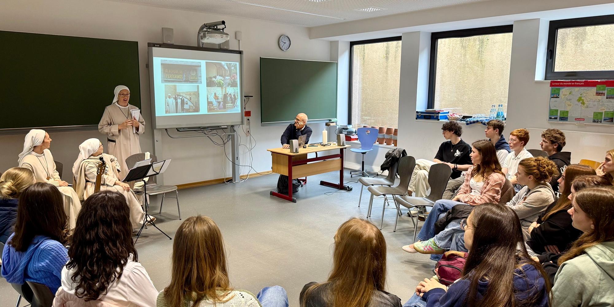 Die spanischen Ordensfrauen berichten im Angela-Merici-Gymnasium über ihr Leben und Wirken. Drei spanische Ordensschwestern beim Vortrag vor einer Klasse.