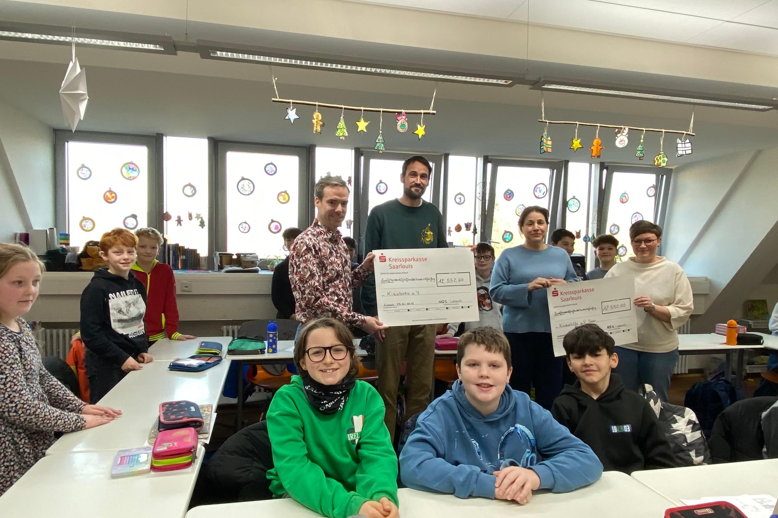 Schülerinnen und Schüler sowie Lehrkräfte der Nikolaus Groß-Schulen in Lebach überreichen Antonia Nutting von Boch (Kinderhilfe Saar) und Lukas Schäfer (Verein Kisoboka, Uganda) symbolisch Schecks mit den Erlösen ihres Spendenlaufs.