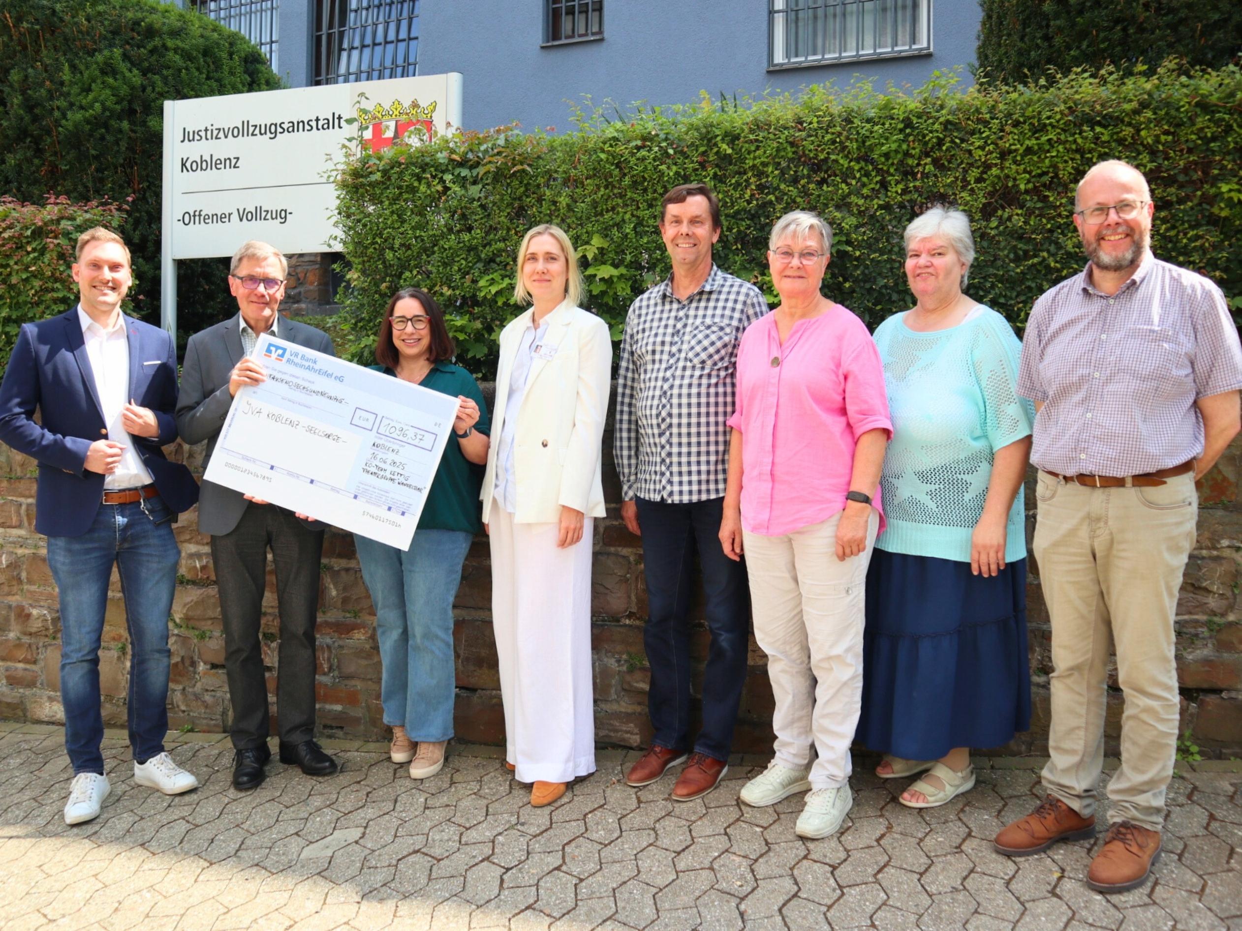 Diakon Frank Lahnstein (Zweiter v. links) freut sich über die Spende des Kirchort-Teams St. Bartholomäus Kettig und der Theatergruppe 'WandelBar' aus Kettig an die katholische Gefängnisseelsorge in der JVA Koblenz. Bei der Scheckübergabe berichten Anstaltsleiter Jörn Omland (links) und die stellvertretende Anstaltsleiterin Carolin Bucksteeg (Vierte v. links) von ihrer Arbeit und dem Alltag in der JVA.