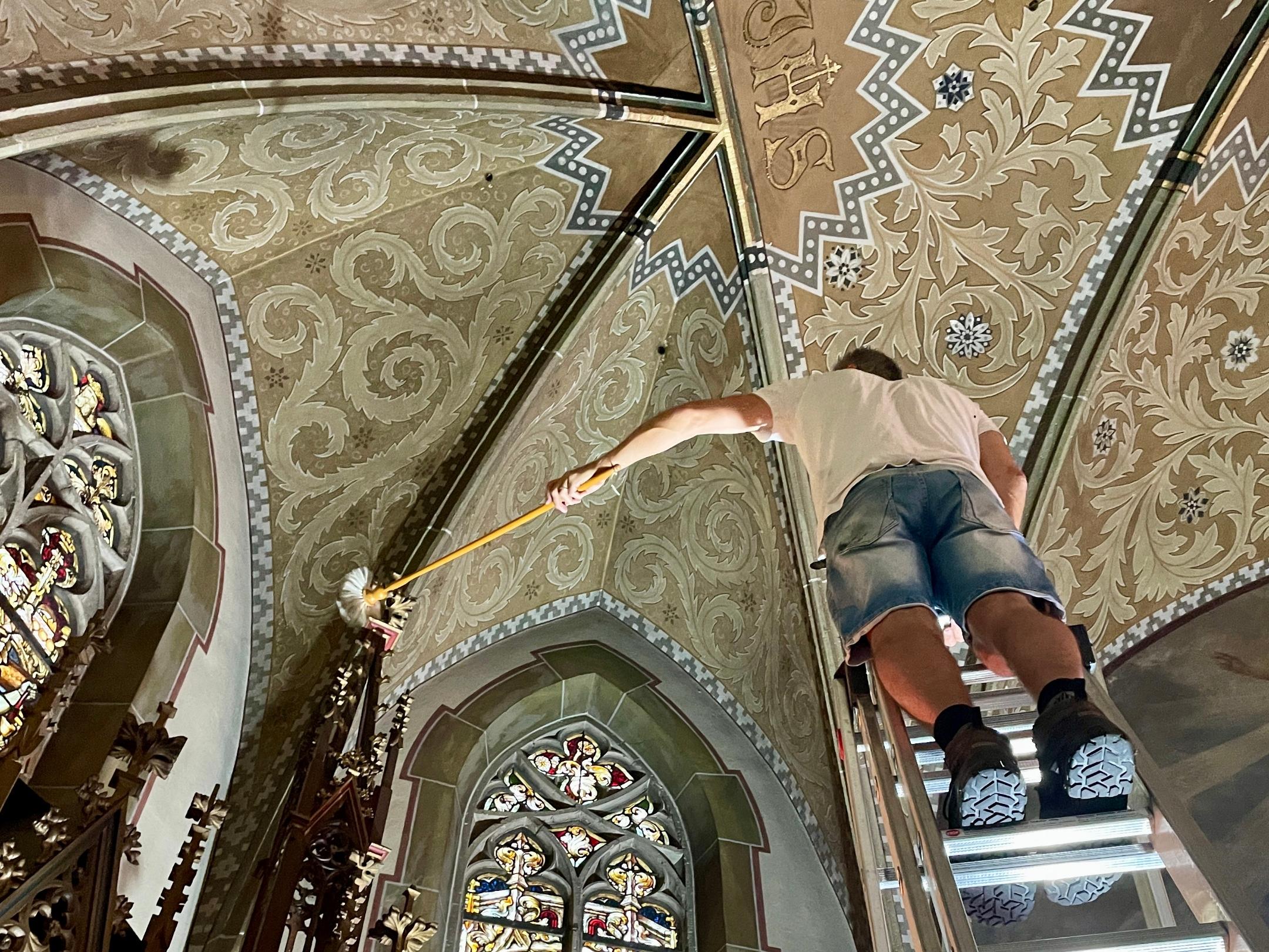 Ein Mann steht in einer Kirche auf einer Leiter vor einem bunten Glasfenster.