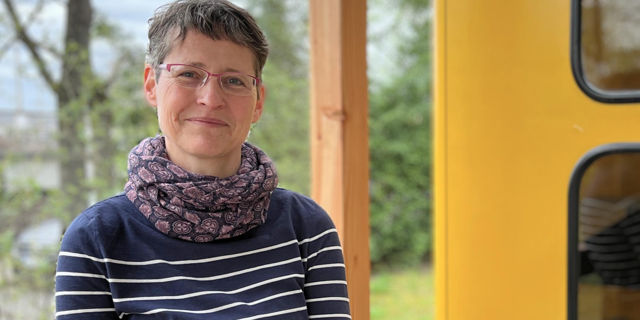 Das Foto zeigt die Protagonistin der Folge, Susanne Schwab. Sie steht im Freien, im Hintergrund sind unscharf Büsche und Bäume zu sehen, rechts ragt eine gelbe Telefonzelle ins Bild. Susanne Schwab trägt einen dunkelblauen Pullover mit hellen Querstreifen, ein Halstuch, Brille, hat kurzgeschnittene, dunkle Haare und schaut lächelnd in die Kamera.