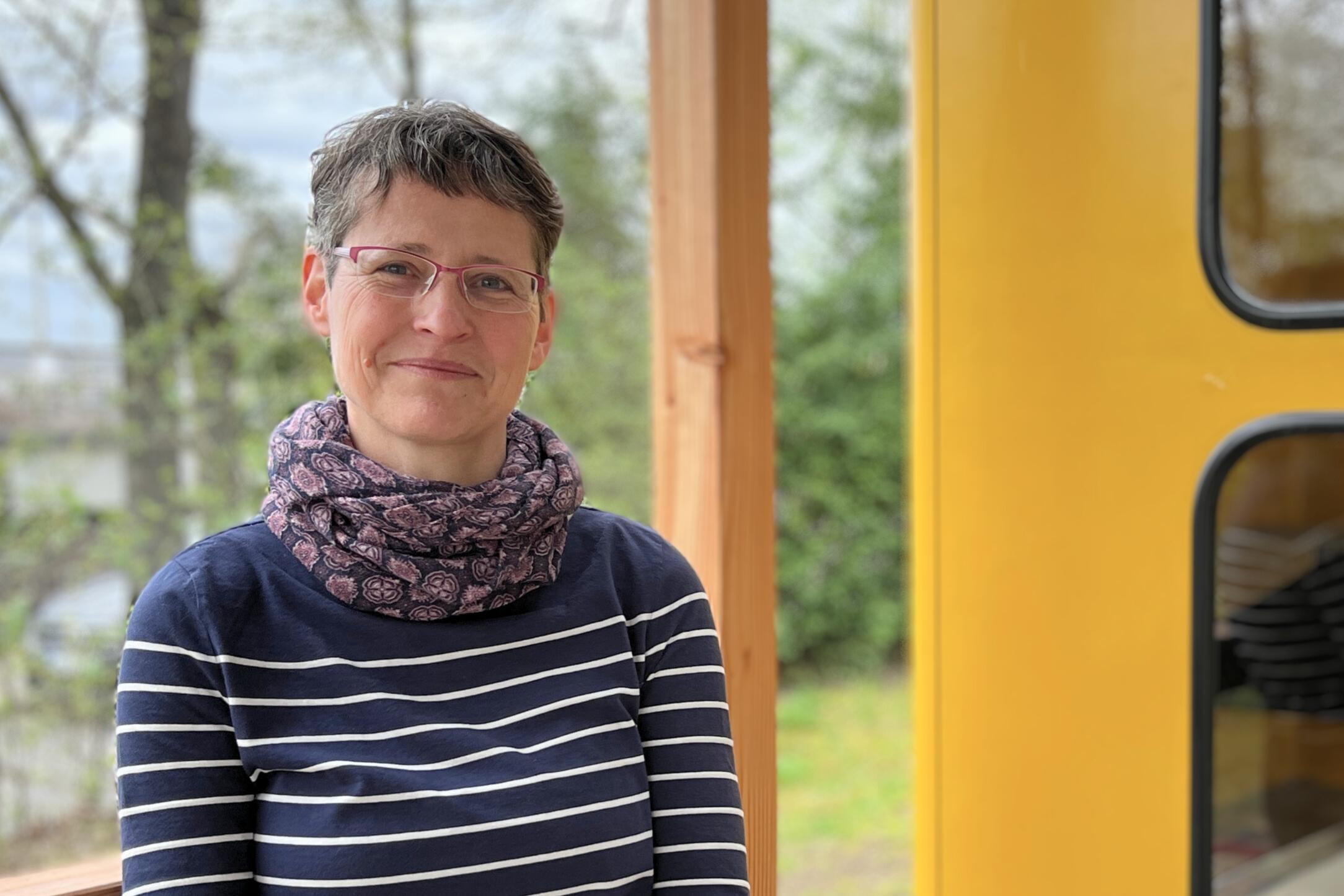 Das Foto zeigt die Protagonistin der Folge, Susanne Schwab. Sie steht im Freien, im Hintergrund sind unscharf Büsche und Bäume zu sehen, rechts ragt eine gelbe Telefonzelle ins Bild. Susanne Schwab trägt einen dunkelblauen Pullover mit hellen Querstreifen, ein Halstuch, Brille, hat kurzgeschnittene, dunkle Haare und schaut lächelnd in die Kamera.
