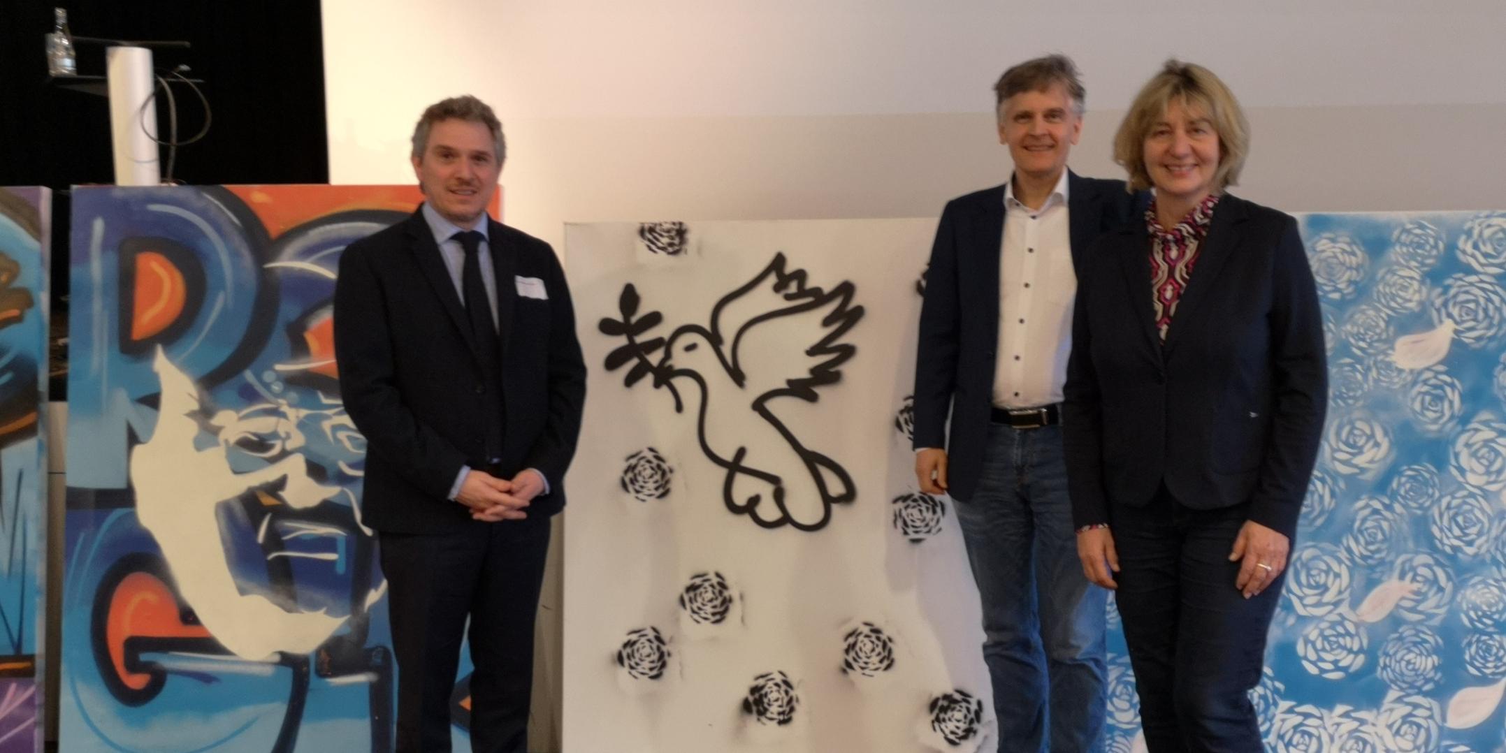 Mit-)Ausrichter PD Dr. Alexander Maier (Fachrichtung Kath. Theologie) und Prof. Dr. Karlo Meyer (Fachrichtung Ev. Theologie) mit Referentin Prof. Dr. Elisabeth Naurath (Universität Augsburg), im Hintergrund einige Streetart-Kunstwerke, die in der Kirche der Jugend eli.ja entstanden.