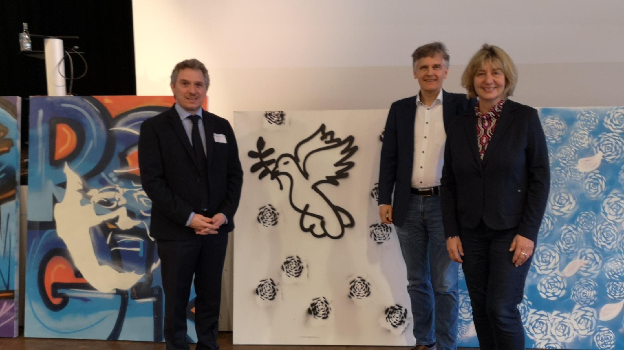 Mit-)Ausrichter PD Dr. Alexander Maier (Fachrichtung Kath. Theologie) und Prof. Dr. Karlo Meyer (Fachrichtung Ev. Theologie) mit Referentin Prof. Dr. Elisabeth Naurath (Universität Augsburg), im Hintergrund einige Streetart-Kunstwerke, die in der Kirche der Jugend eli.ja entstanden.
