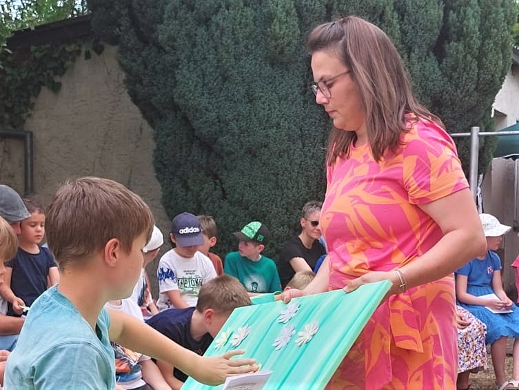 Ein Kommunionkind klebt eine Papierblüte auf; rechts Gemeindereferentin Tamara Müller