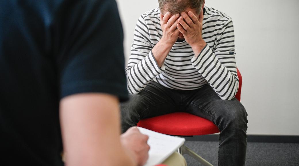 Patient sitzt auf Stuhl und hält sich den Kopf.