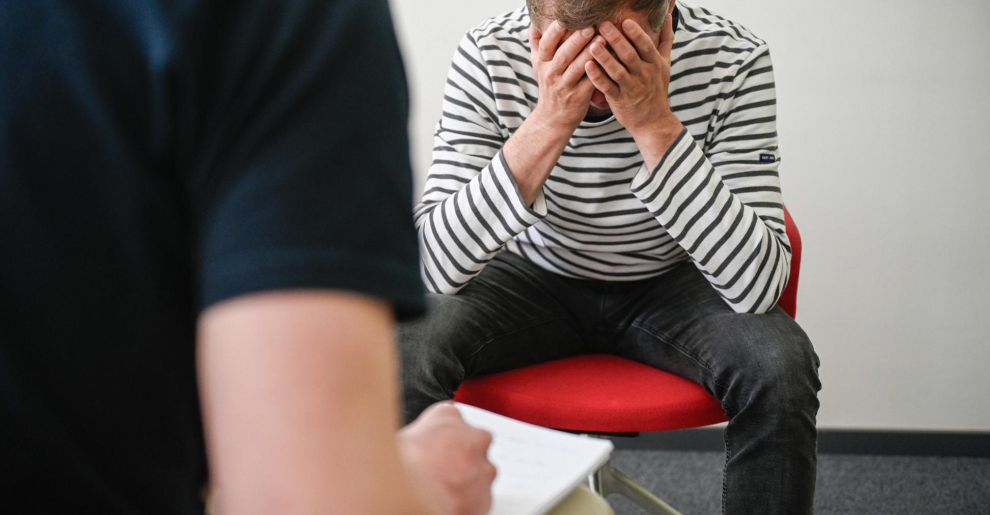 Patient sitzt auf Stuhl und hält sich den Kopf.