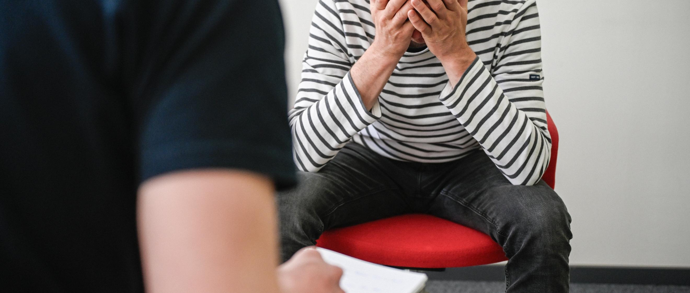 Patient sitzt auf Stuhl und hält sich den Kopf.
