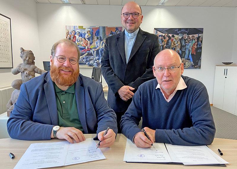 Dezernent Markus Nöhl (links), der Pfarrer der Pfarrei Liebfrauen, Dr. Markus Nicolay (stehend) und Thomas Schiffler, Vorsitzender des Verwaltungsrates der Pfarrei, bei der Unterzeichnung des Vertrags mit der die Pfarrei Liebfrauen künftig auf die Zahlung der Zinsen aus dem Nachlass von Dr. Dietrich Flade verzichten wird.