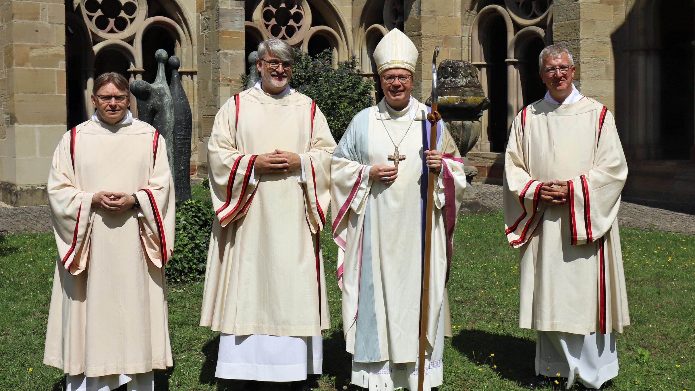 Vier Männer (Priester, Diakon, Bischof) stehen auf der Wiese am Trierer Dom