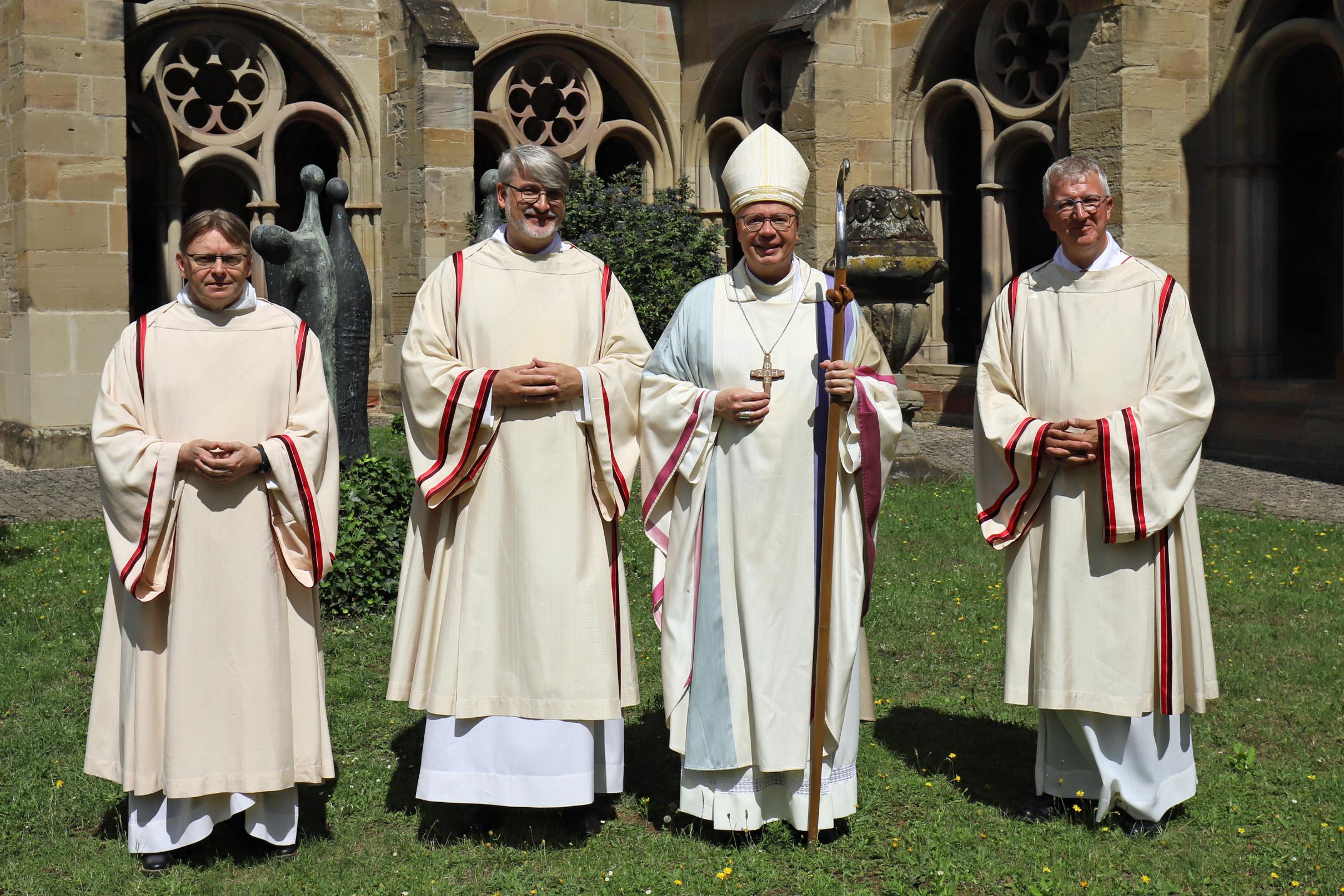 Vier Männer (Priester, Diakon, Bischof) stehen auf der Wiese am Trierer Dom