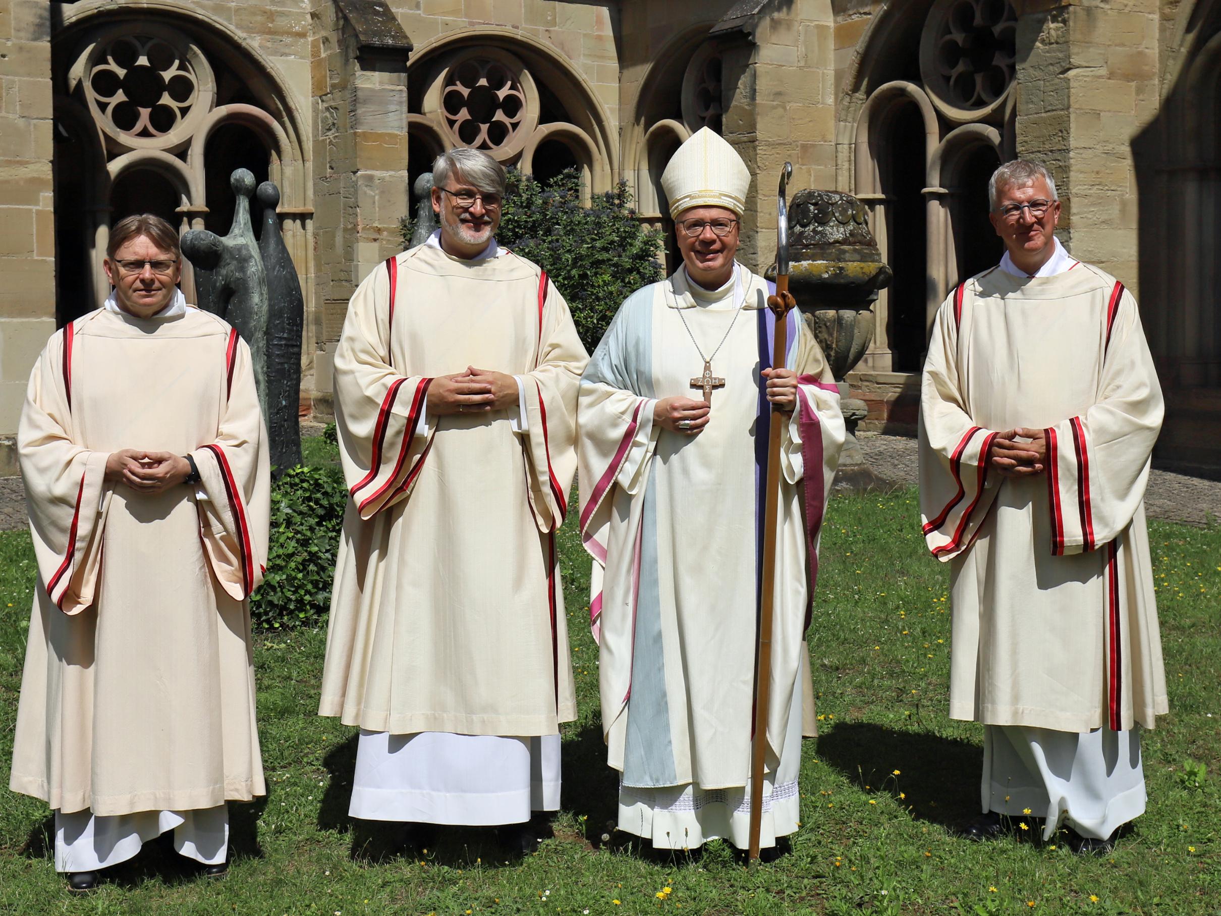 Vier Männer (Priester, Diakon, Bischof) stehen auf der Wiese am Trierer Dom