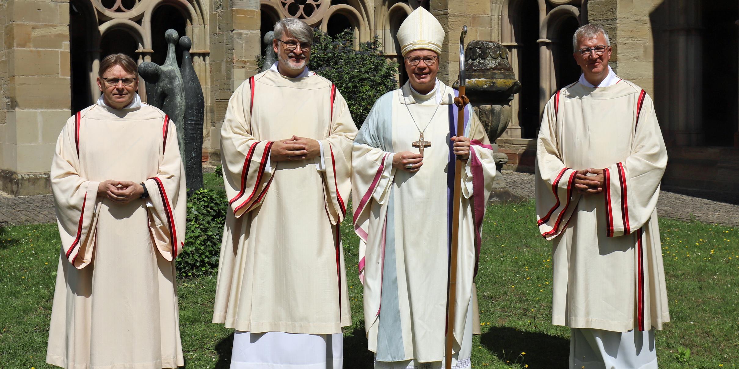 Vier Männer (Priester, Diakon, Bischof) stehen auf der Wiese am Trierer Dom