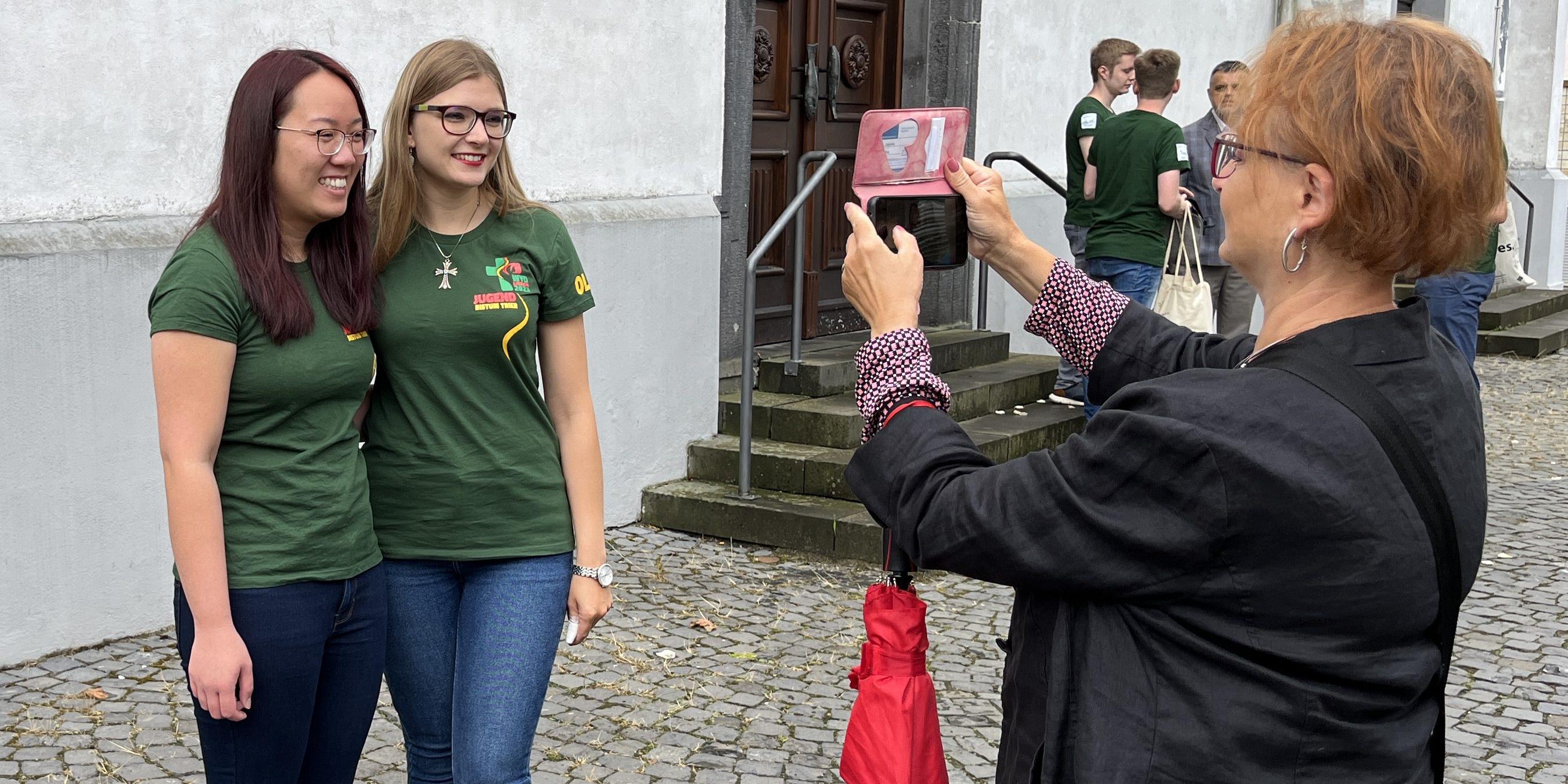 Zwei Mädchen stehen vor einer Frau, die mit einem Handy ein Foto macht.