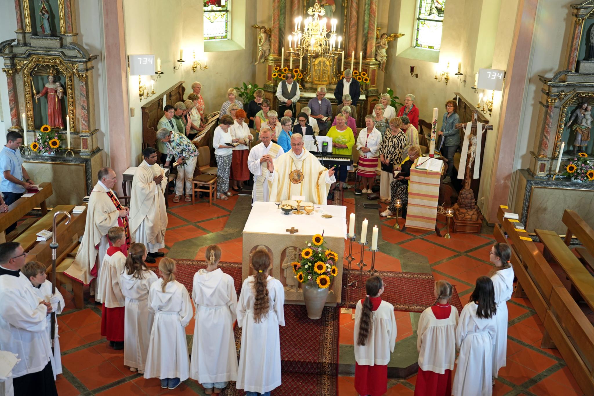Weihbischof Peters, ein Chor sowie Messdienerinnen und Messdiener feiern Gottesdienst in der Kirche in Faid.