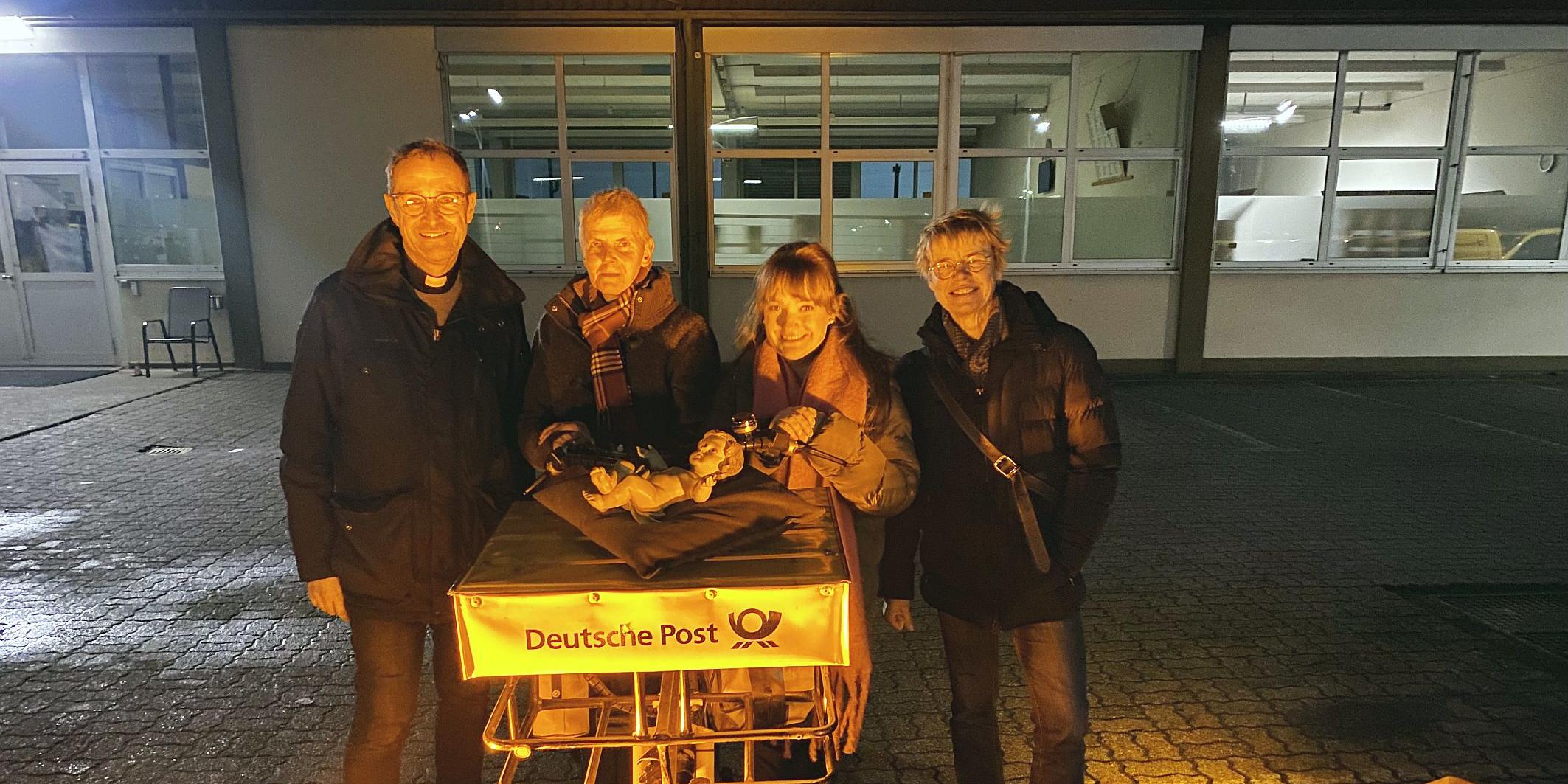 Pfarrer Jörg Meyrer, Ulrike Phiesel, Nadine Kreuser und Bärbel Knieps vom Vorbereitungsteam mit der Figur des Jesuskinds, das von einem Postboten per Fahrrad geliefert wurde.