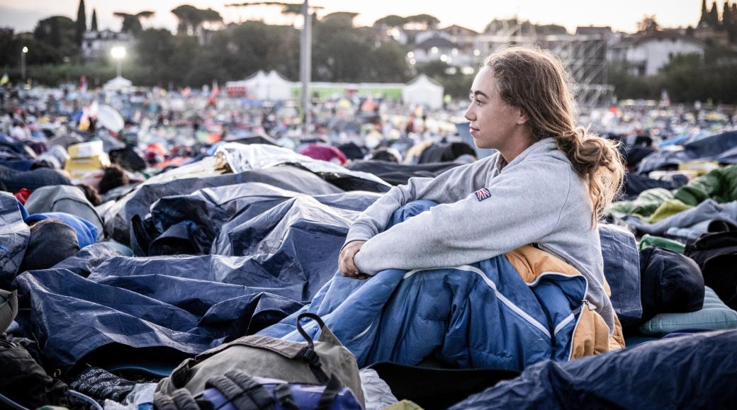 Am Morgen nach der Gebetsnacht beim Weltjugendtreffen 2025 in Rom: Eine junge Frau sitzt in ihrem Schlafsack und blickt über das Gelände.