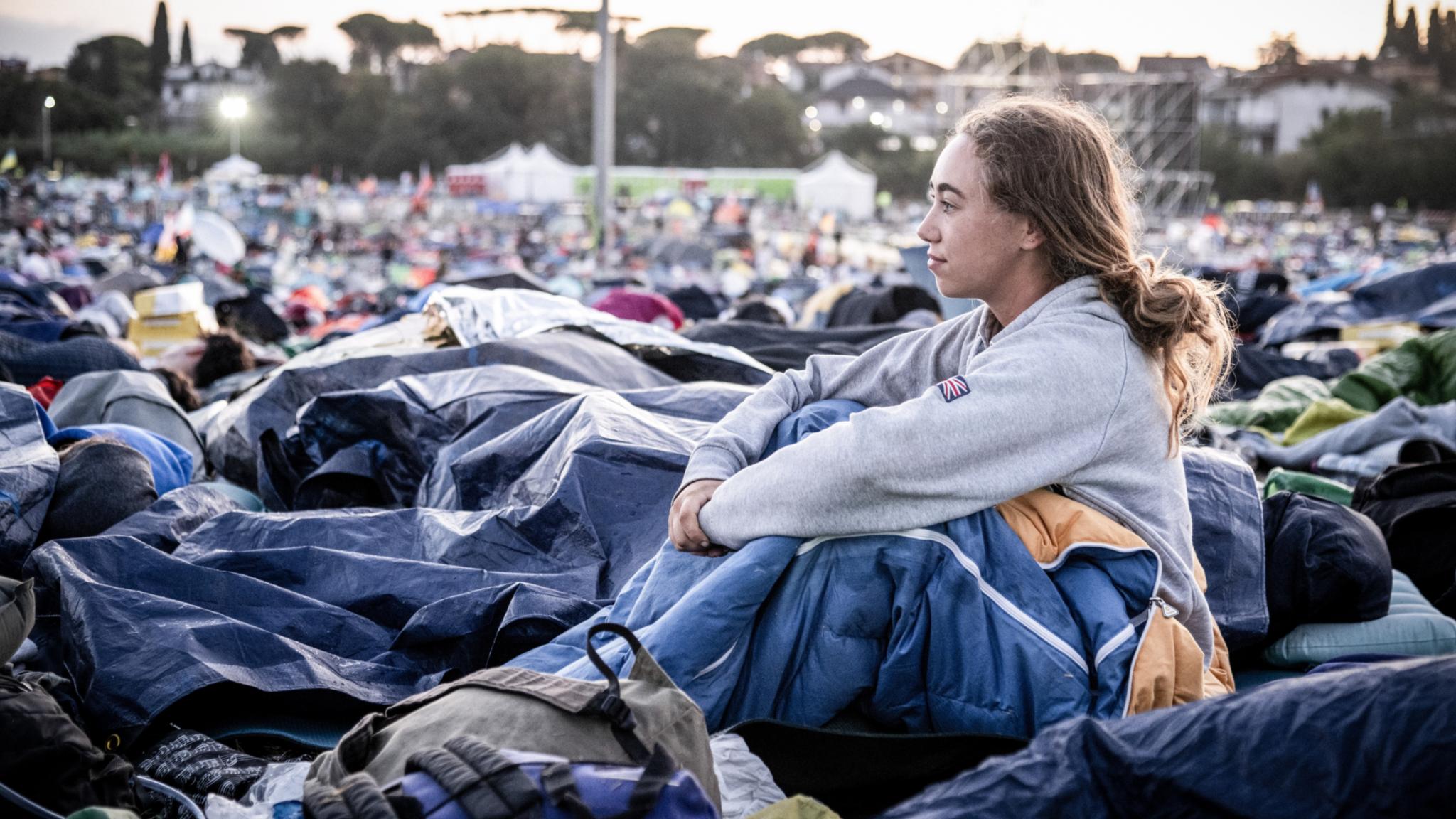 Am Morgen nach der Gebetsnacht beim Weltjugendtreffen 2025 in Rom: Eine junge Frau sitzt in ihrem Schlafsack und blickt über das Gelände.