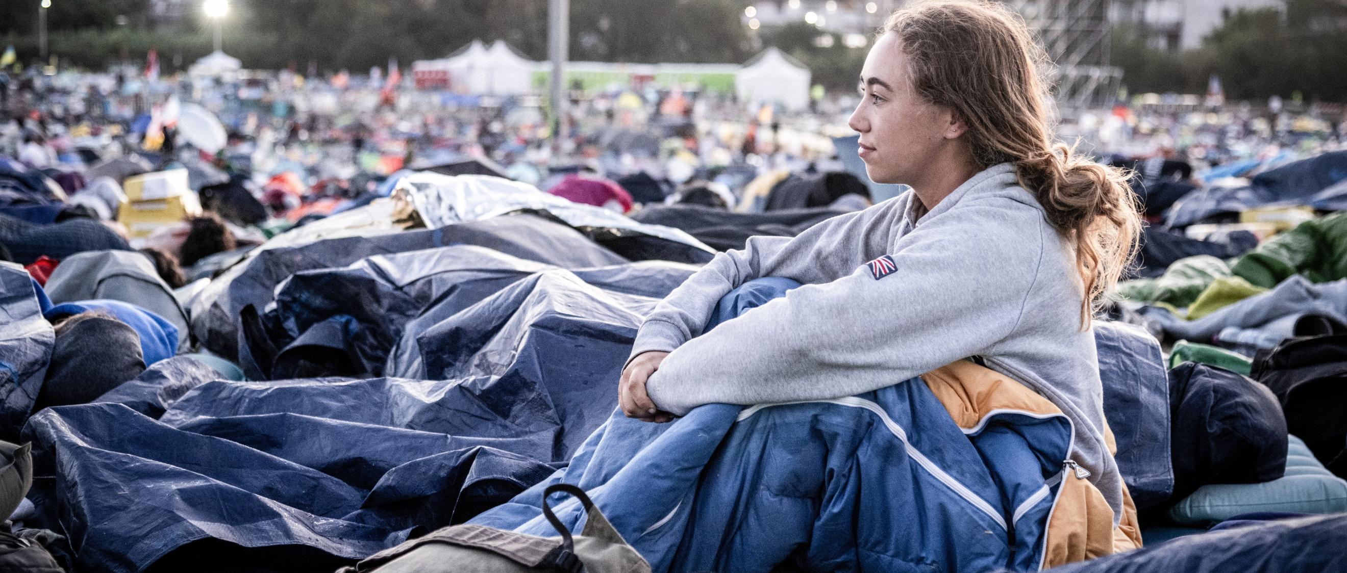 Am Morgen nach der Gebetsnacht beim Weltjugendtreffen 2025 in Rom: Eine junge Frau sitzt in ihrem Schlafsack und blickt über das Gelände.