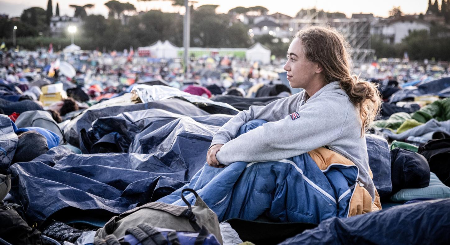 Am Morgen nach der Gebetsnacht beim Weltjugendtreffen 2025 in Rom: Eine junge Frau sitzt in ihrem Schlafsack und blickt über das Gelände.