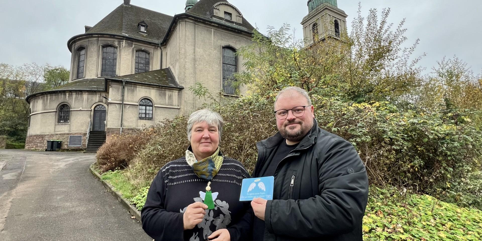 Zwei Menschen stehen vor einer Kirche und präsentieren eine Karte, die sie in der Hand halten