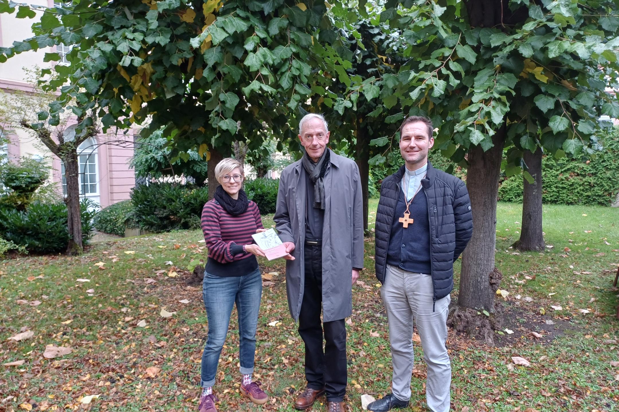 Julia Lehn und Peter Zillgen (rechts) übergeben ein Exemplar des Zeitzeugen-Bandes an Domkapitular und Interviewpartner Benedikt Welter.