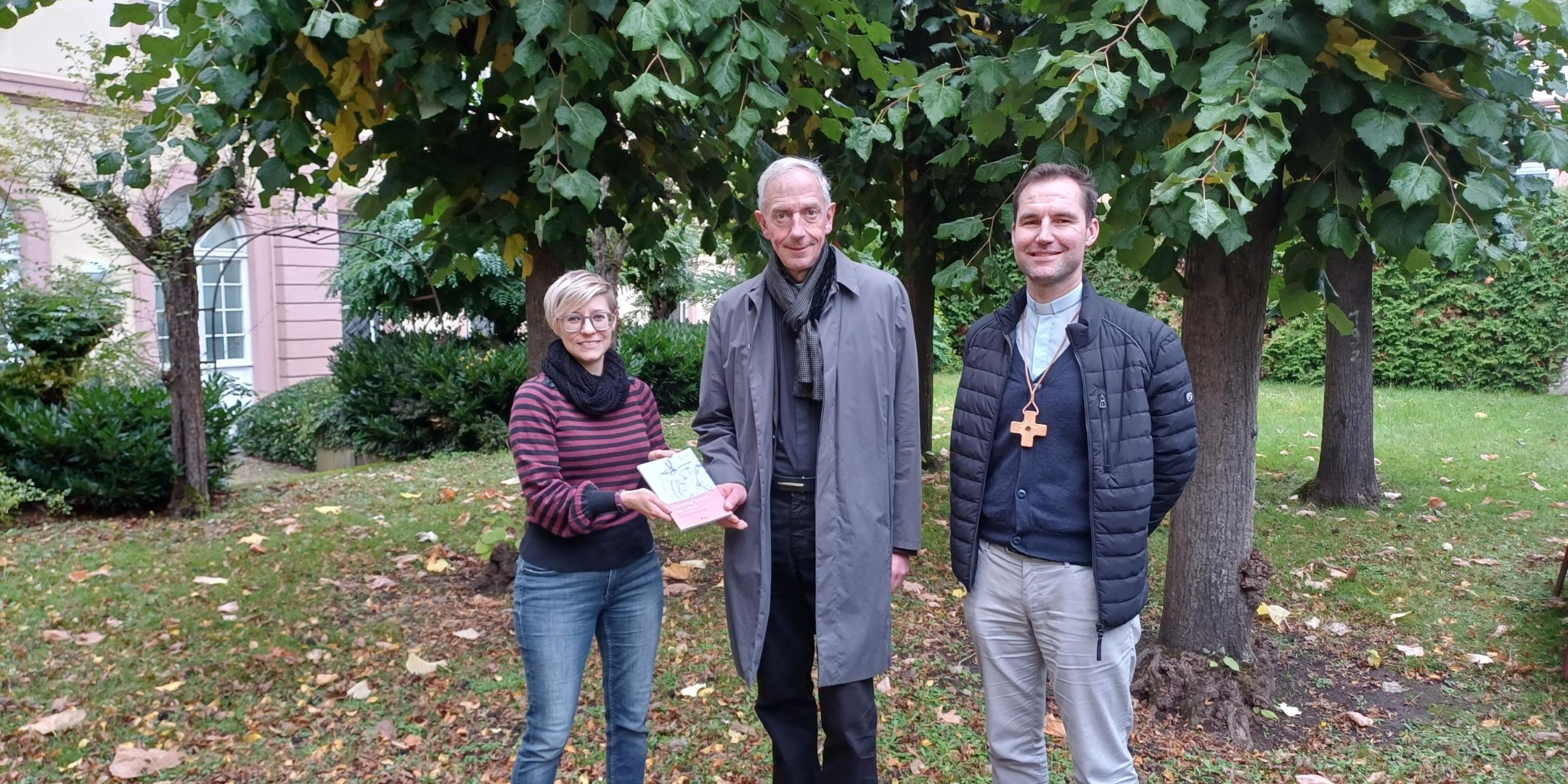 Julia Lehn und Peter Zillgen (rechts) übergeben ein Exemplar des Zeitzeugen-Bandes an Domkapitular und Interviewpartner Benedikt Welter.