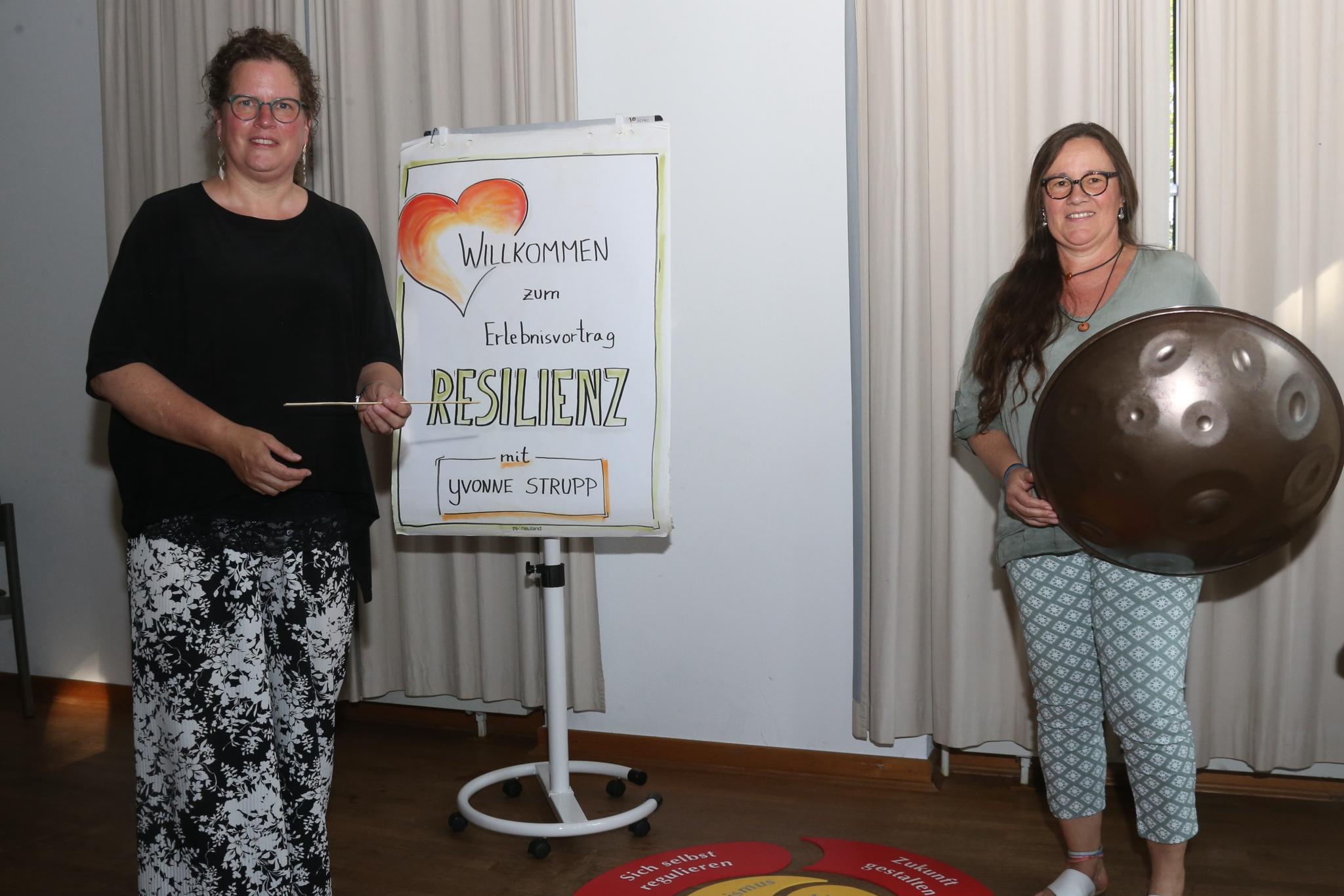 Zwei Frauen, eine mit Handpan, vor einer Pinnwand