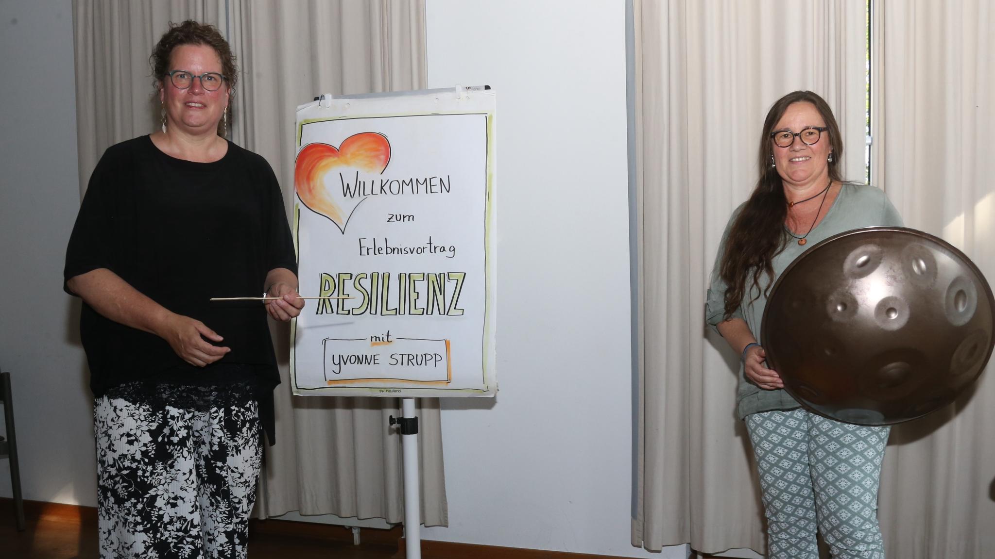 Zwei Frauen, eine mit Handpan, vor einer Pinnwand