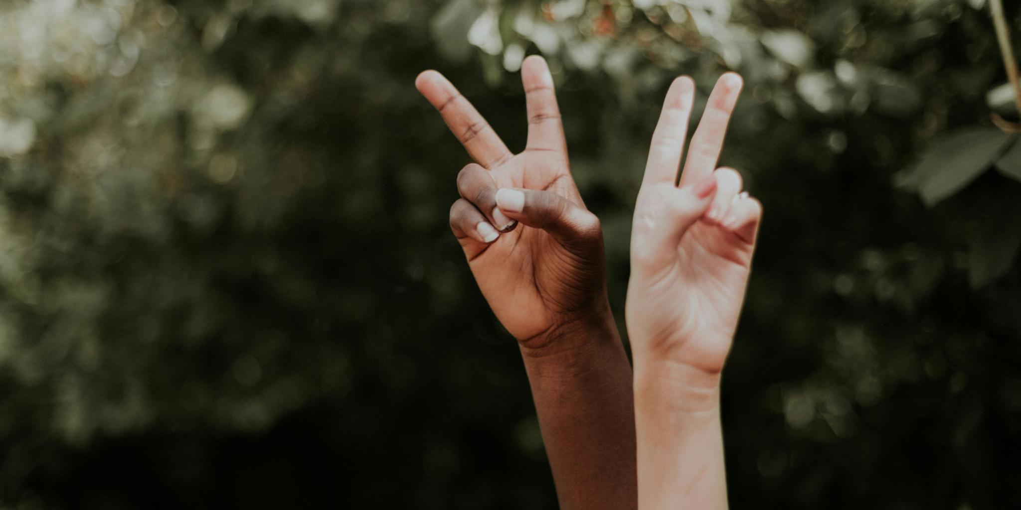 Hände von zwei Personen, die das Peace-Zeichen mit den Fingern formen.