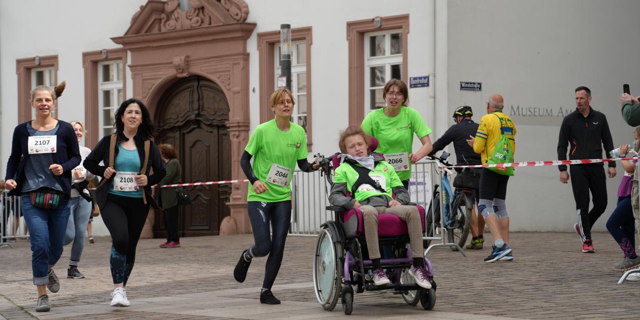 Fünf Menschen, davon eine Person im Rollstuhl, laufen über die Strecke
