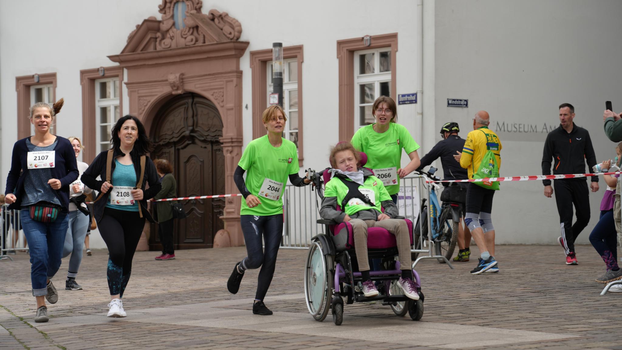 Fünf Menschen, davon eine Person im Rollstuhl, laufen über die Strecke