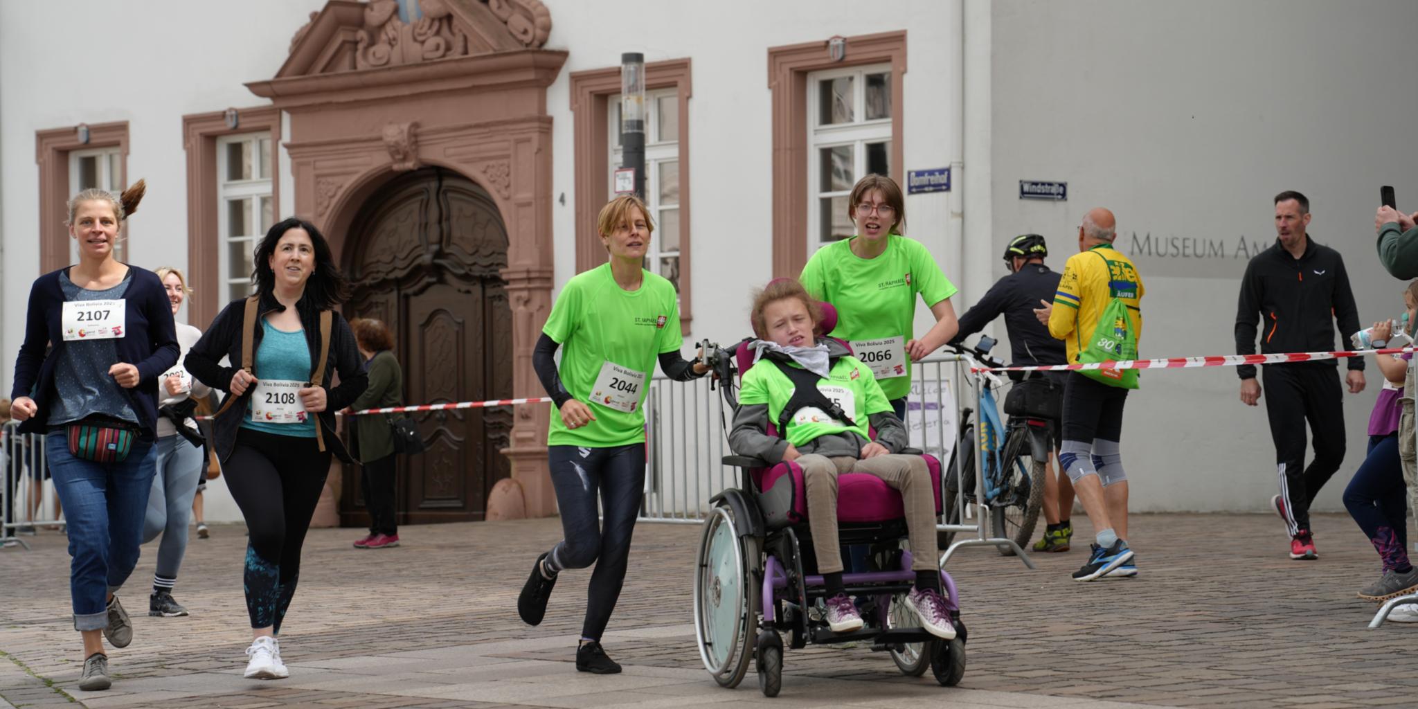 Fünf Menschen, davon eine Person im Rollstuhl, laufen über die Strecke