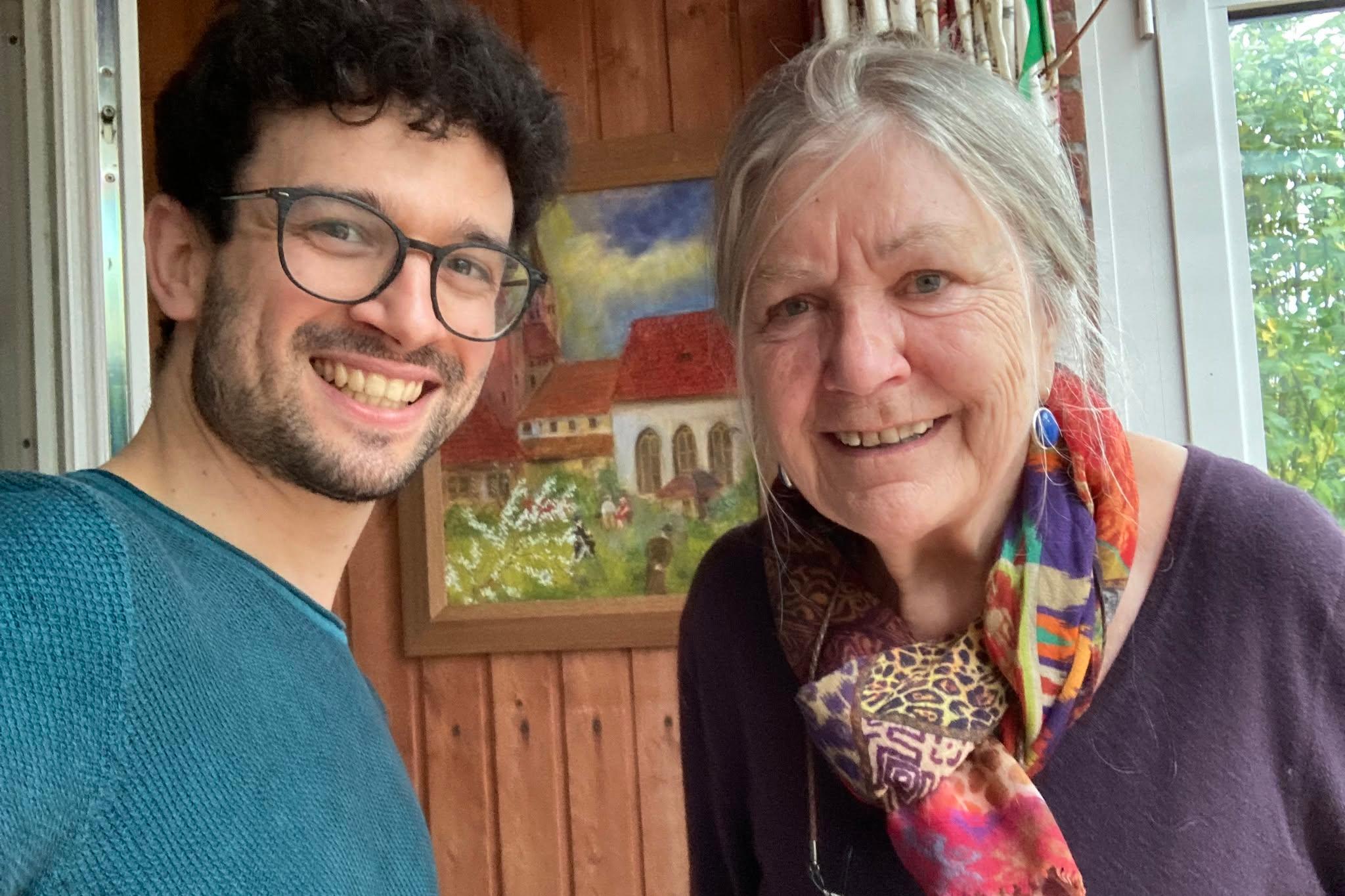 Ein Mann mit dunklen Locken und Brille und eine ältere Frau lächeln in die Kamera