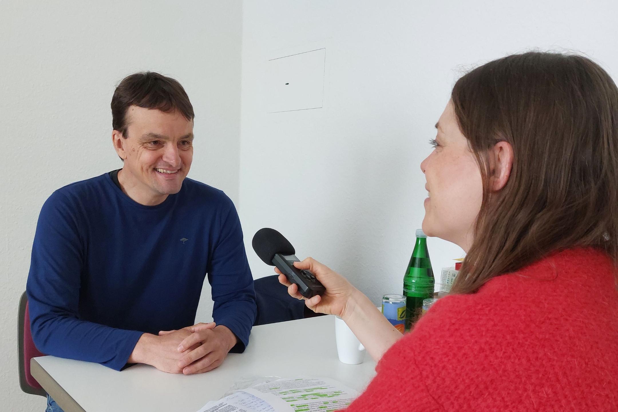 Ein Mann sitzt mit einer Frau am Tisch und sie unterhalten sich mit einem Mikrofon für die Podcastaufnahme