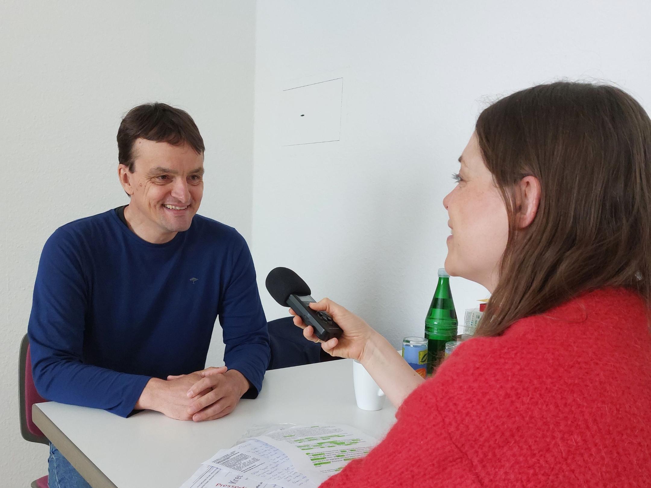 Ein Mann sitzt mit einer Frau am Tisch und sie unterhalten sich mit einem Mikrofon für die Podcastaufnahme