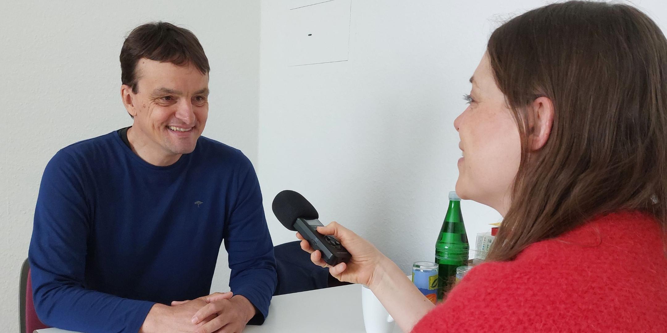 Ein Mann sitzt mit einer Frau am Tisch und sie unterhalten sich mit einem Mikrofon für die Podcastaufnahme