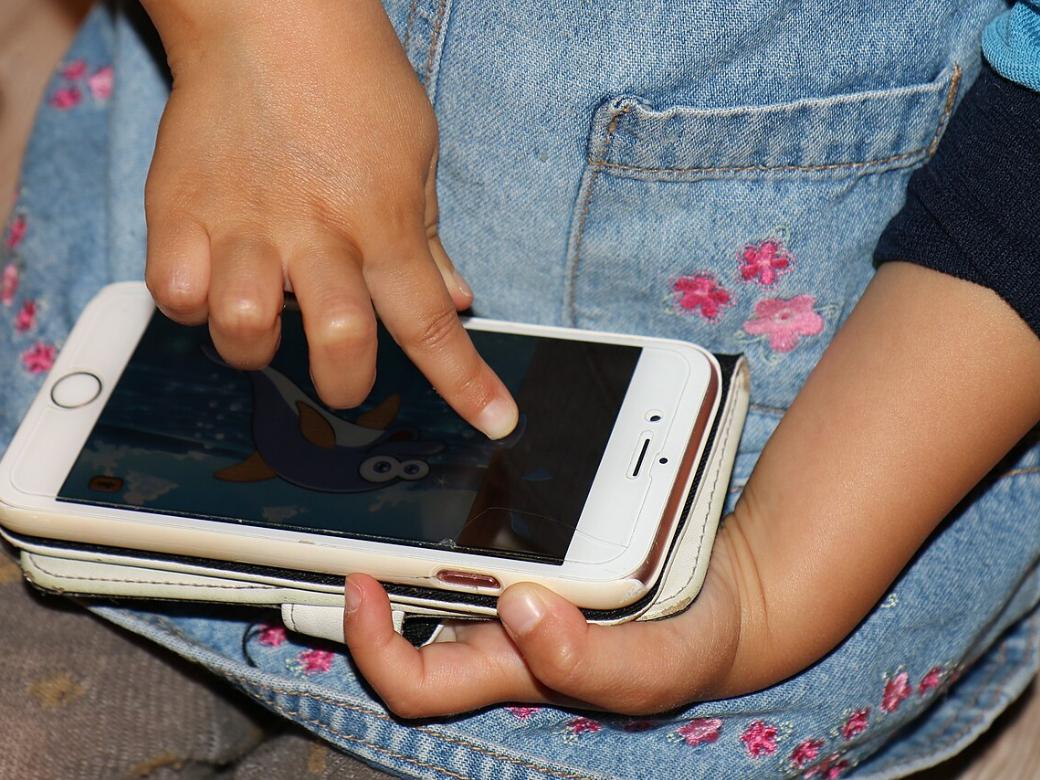 Eine Kinderhand tippt auf einem Smartphone