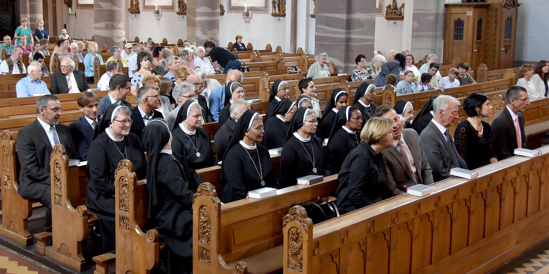Schwestern und Kirchenbesucher auf Kirchenbänlen sitzend