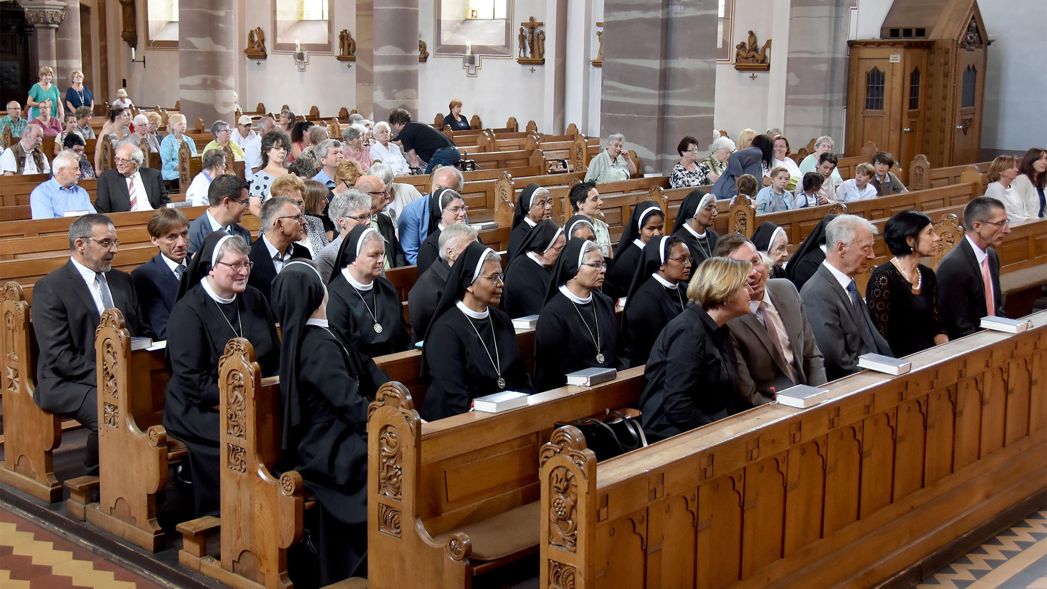 Schwestern und Kirchenbesucher auf Kirchenbänlen sitzend