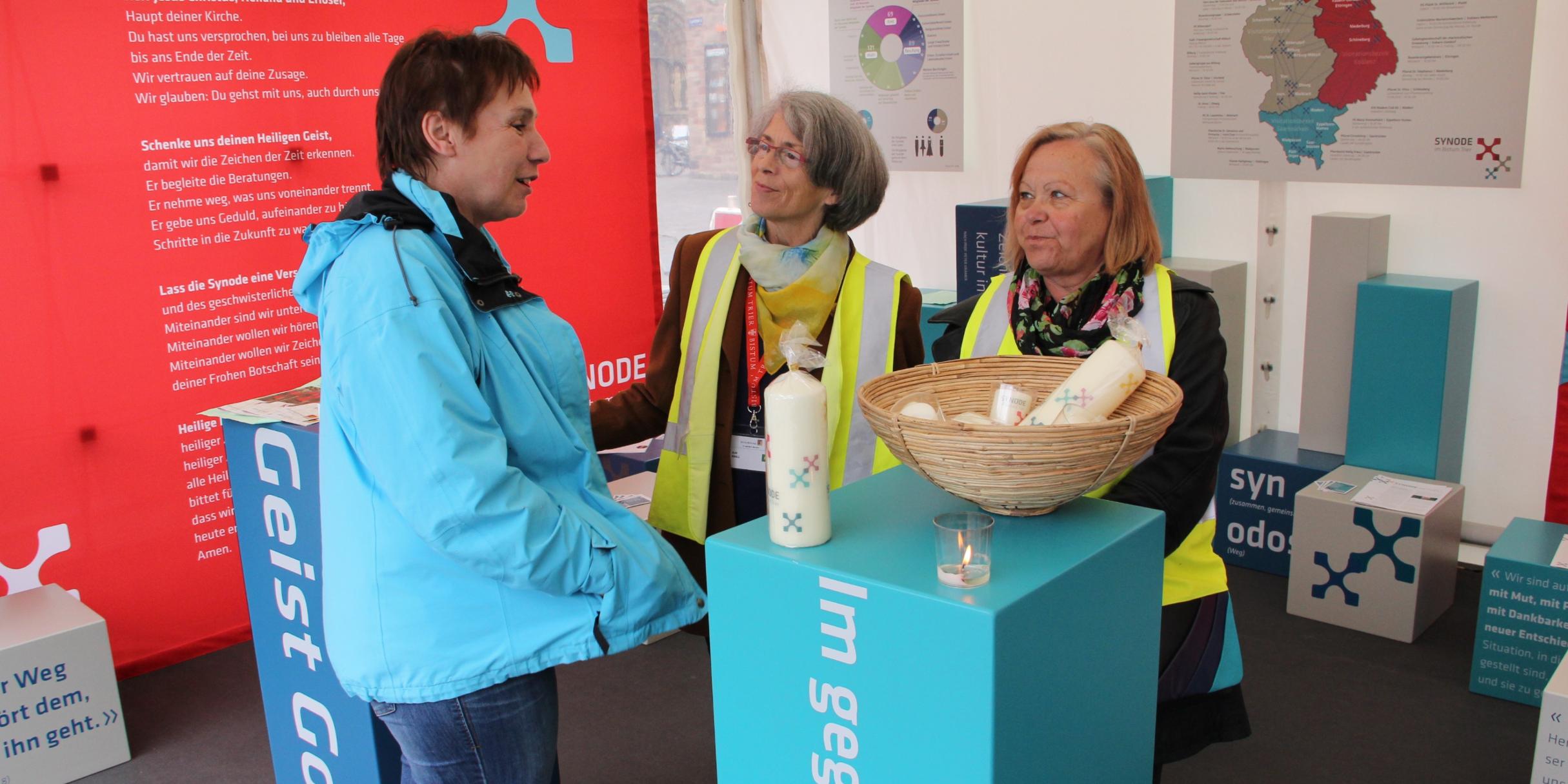 Helferinnen des Bistum Trier mit eingepackten Kerzen und rot/weißer Werbung für das Bistum im Hintergrund