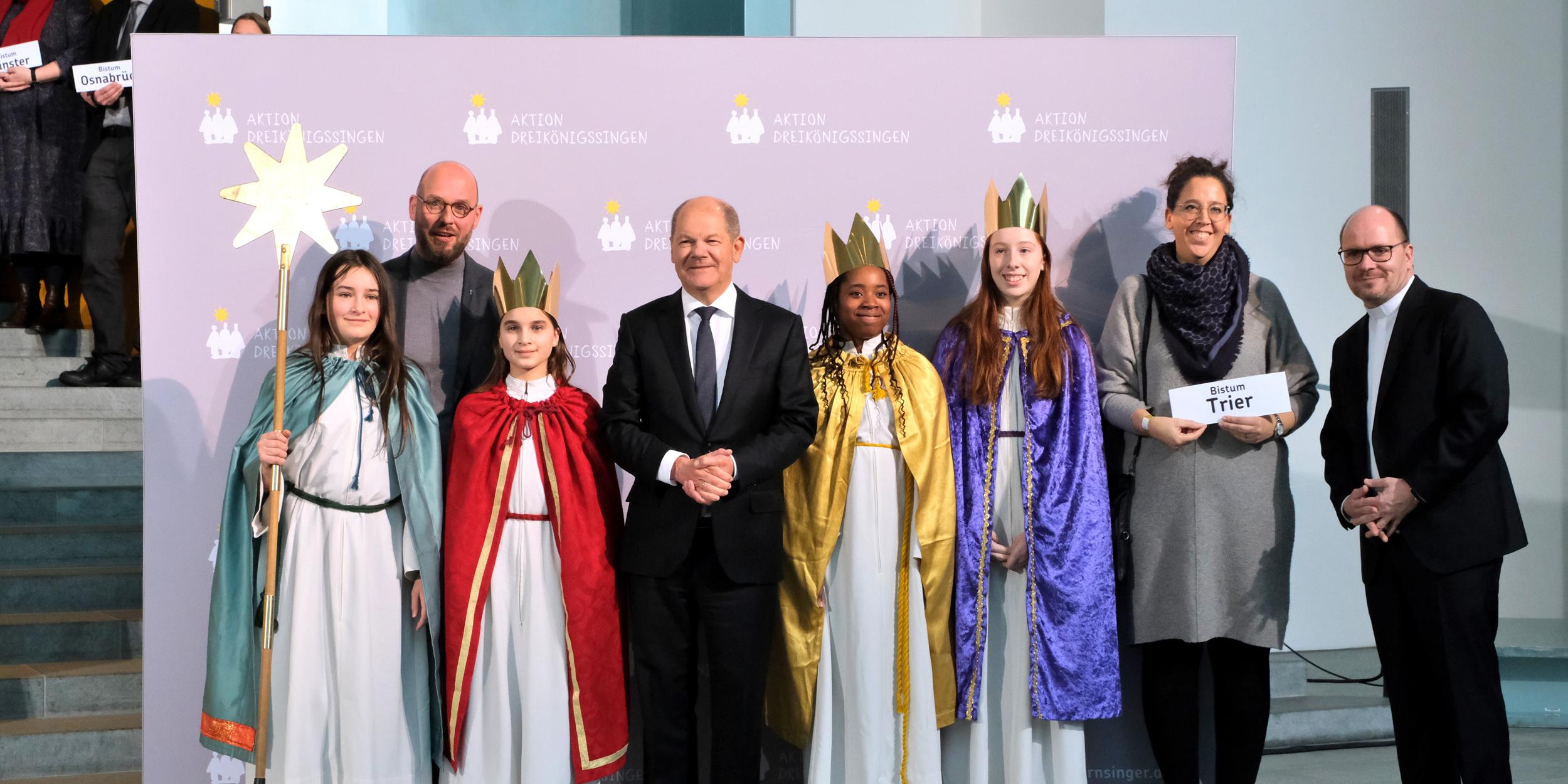 Die Sternsingerinnen Daphne (12), Sophia (12), Mia (11) und Regina (11) sowie Begleiterin Mirjam Nayman aus der Pfarrei St. Martin in Merzig-Bietzen vertraten das Bistum Trier am Donnerstagnachmittag beim Sternsinger-Empfang von Bundeskanzler Olaf Scholz zur 65. Aktion Dreikönigssingen. Zum Gruppenfoto mit dem Kanzler stellten sie sich gemeinsam mit Pfarrer Dirk Bingener, Präsident des Kindermissionswerks ‚Die Sternsinger‘, und Domvikar Stefan Ottersbach, Bundespräses des Bundes der Deutschen Katholischen Jugend (BDKJ), im Bundeskanzleramt auf. Foto: Ralf Adloff/ Kindermissionswerk