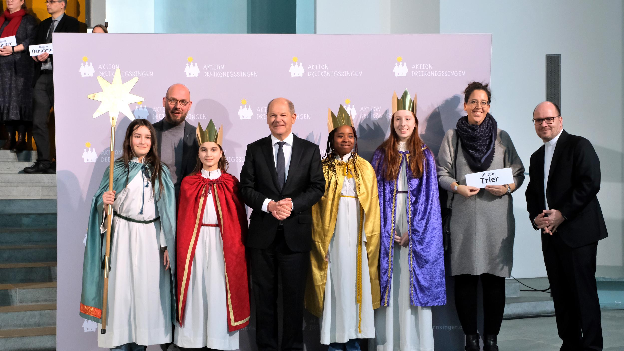 Die Sternsingerinnen Daphne (12), Sophia (12), Mia (11) und Regina (11) sowie Begleiterin Mirjam Nayman aus der Pfarrei St. Martin in Merzig-Bietzen vertraten das Bistum Trier am Donnerstagnachmittag beim Sternsinger-Empfang von Bundeskanzler Olaf Scholz zur 65. Aktion Dreikönigssingen. Zum Gruppenfoto mit dem Kanzler stellten sie sich gemeinsam mit Pfarrer Dirk Bingener, Präsident des Kindermissionswerks ‚Die Sternsinger‘, und Domvikar Stefan Ottersbach, Bundespräses des Bundes der Deutschen Katholischen Jugend (BDKJ), im Bundeskanzleramt auf. Foto: Ralf Adloff/ Kindermissionswerk