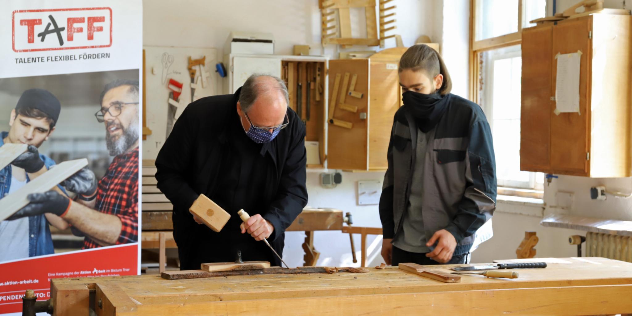 Bischof Ackermann und Marlon schreinern gemeinsam ein Holzkreuz.
