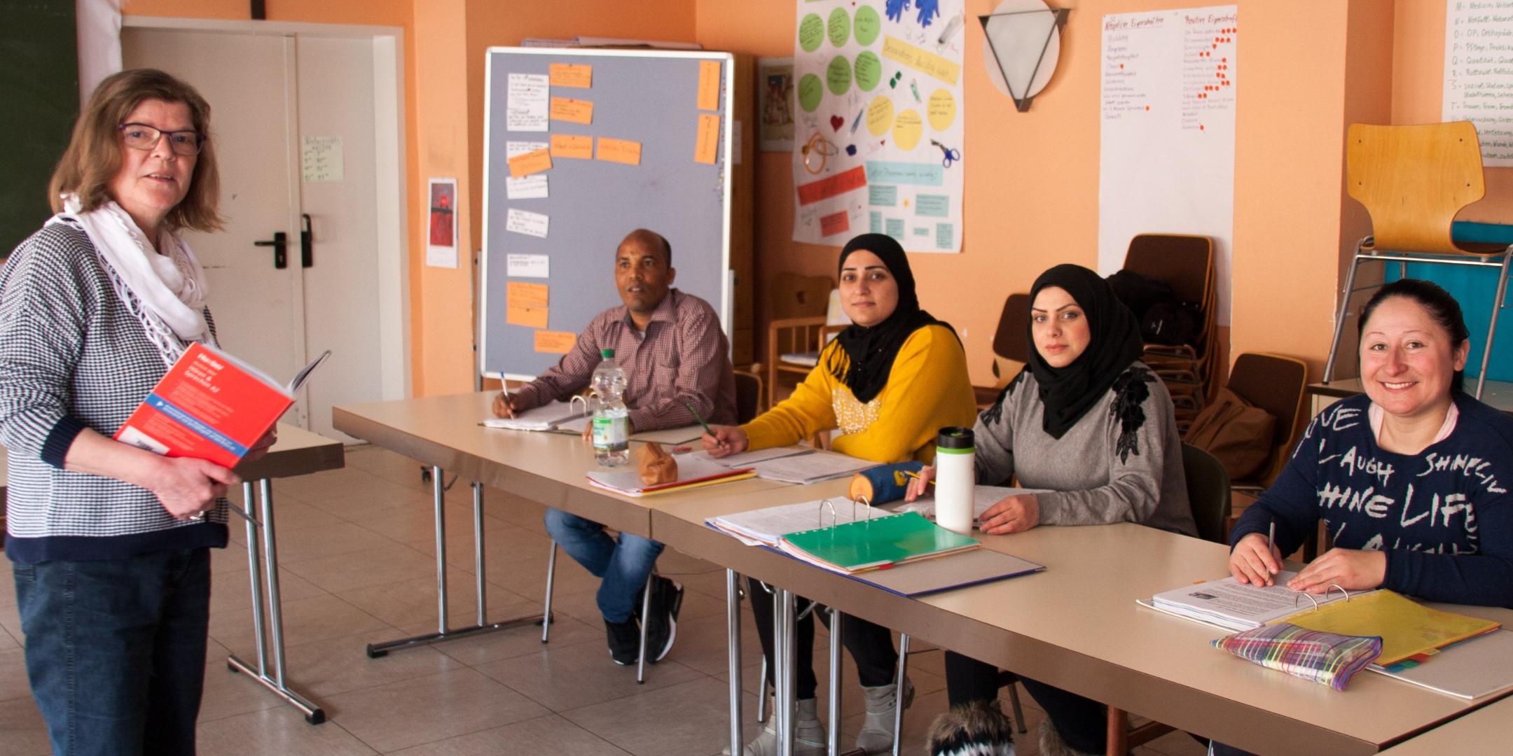Ulrike Kögel (stehend) unterstützt Amanuel, Fatima, Haifa und Emel (v. hinten nach vorne) beim Schulabschluss