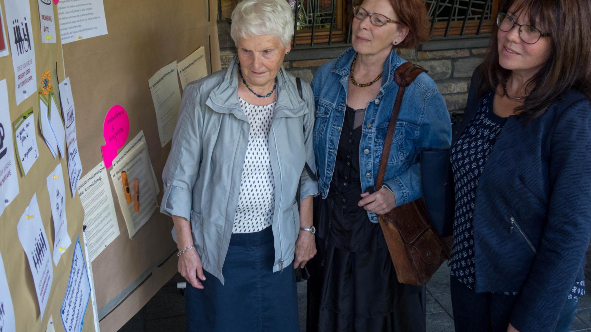 Sigrid Becker, Katharina Berger und die Gemeindereferentin Andrea Ulrich (v. links) schauen sich eine Infotafel zum „Rat der Pfarrei“ an.