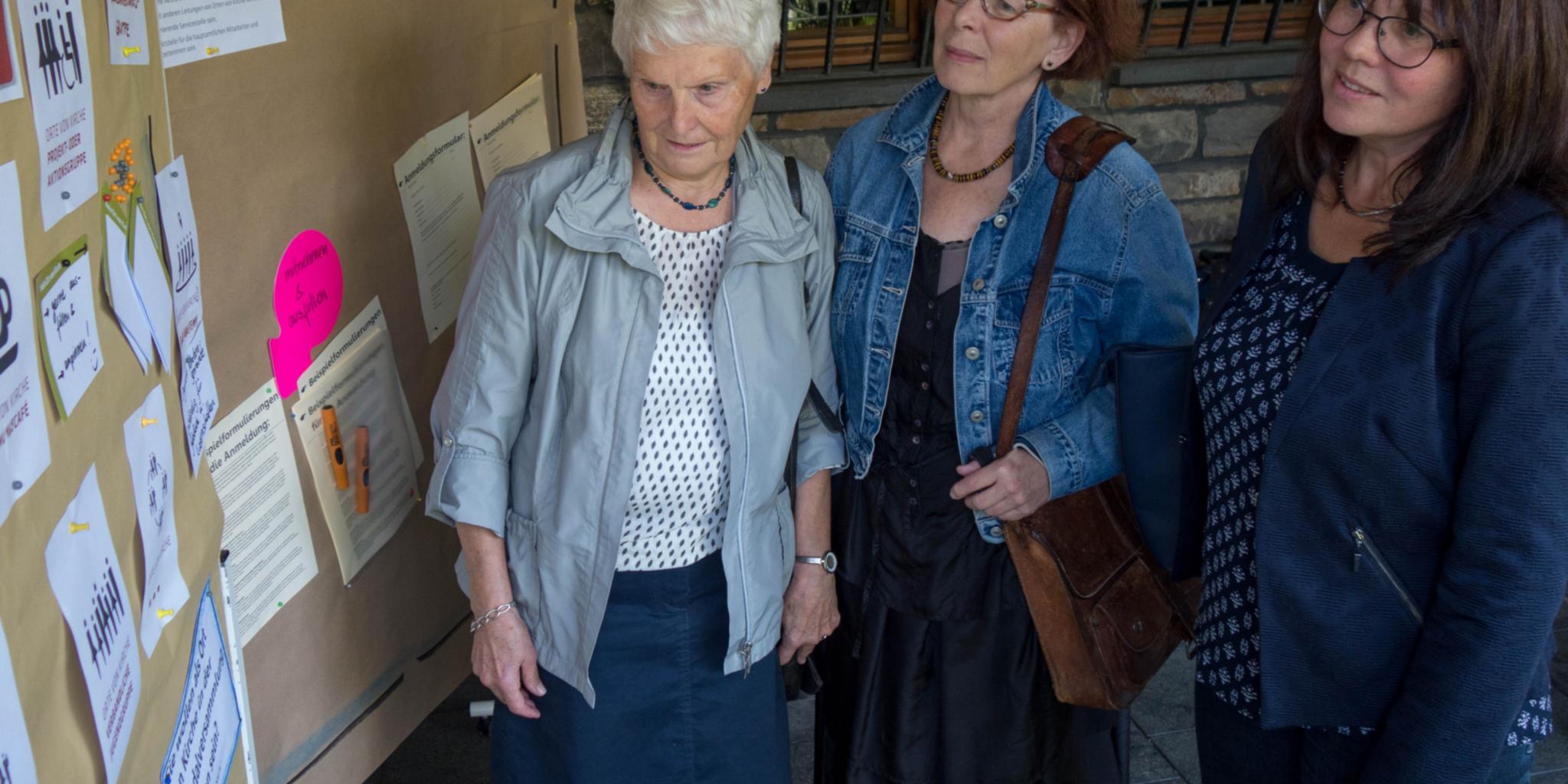 Sigrid Becker, Katharina Berger und die Gemeindereferentin Andrea Ulrich (v. links) schauen sich eine Infotafel zum „Rat der Pfarrei“ an.