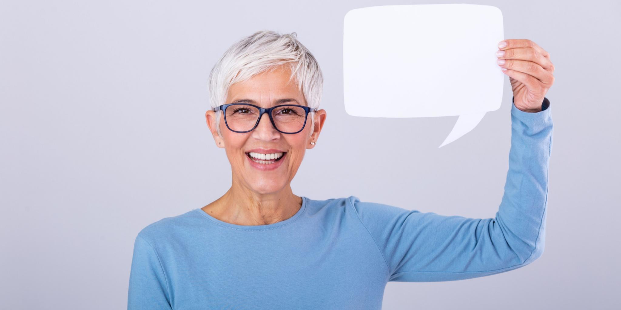 Frau mit grauen Haaren hält Schild in Form von Sprechblase