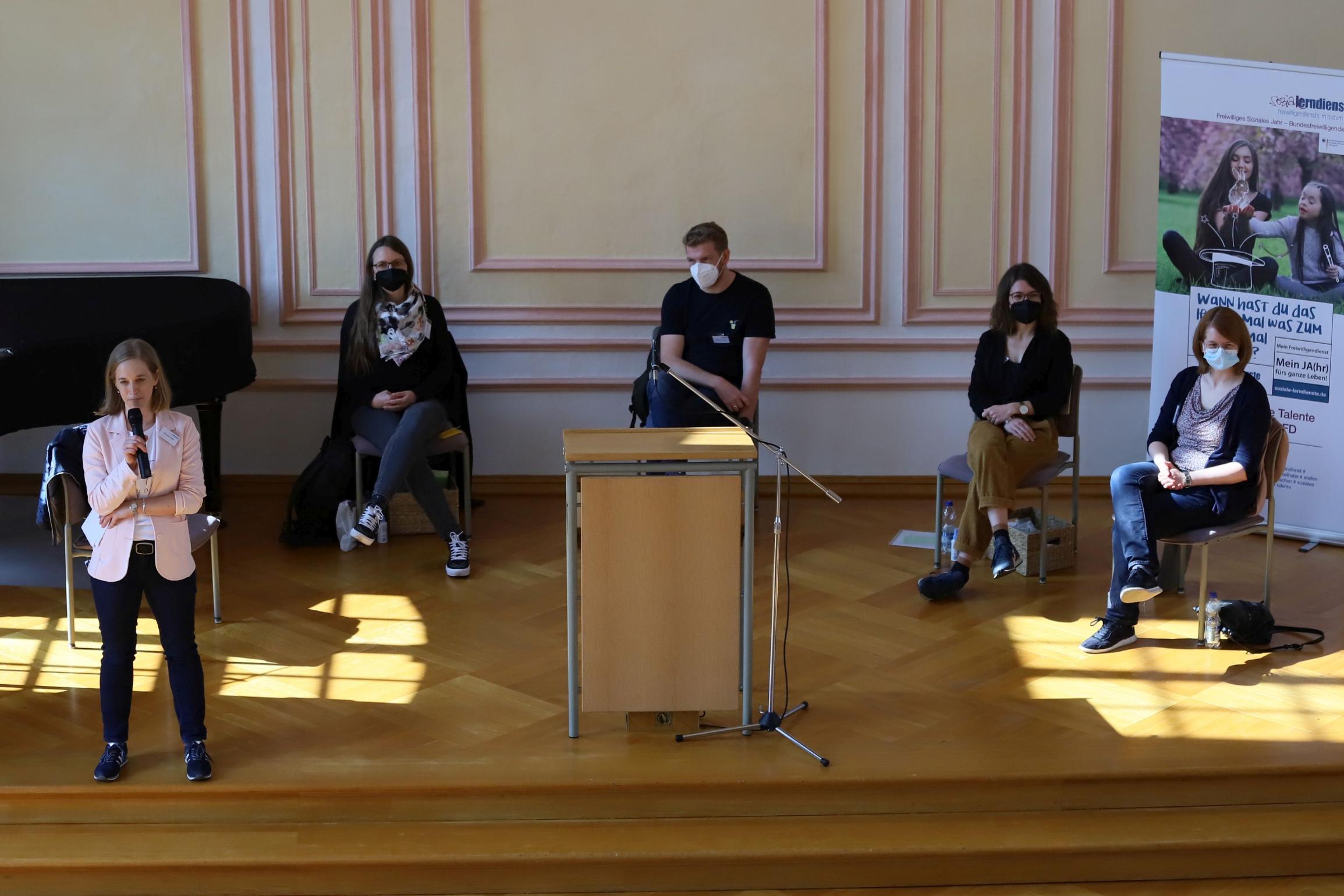 Die Leiterin Susanne Kiefer am Mikro, im Hintergrund das Vorbereitungsteam des Tages. (Foto: Simone Bastreri/Bistum Trier)