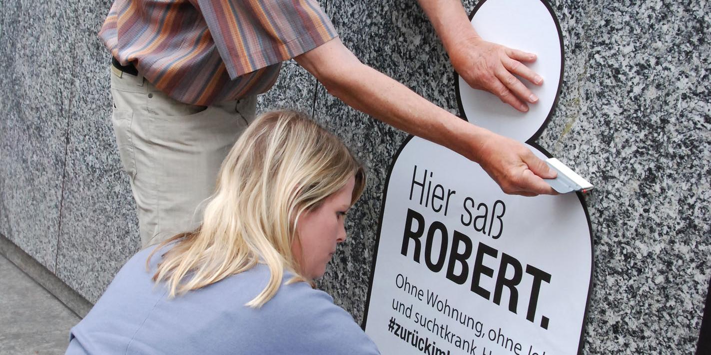 Sozialarbeiterin Sarah Jochum und Bewohner Holger Becker kleben das erste Plakat